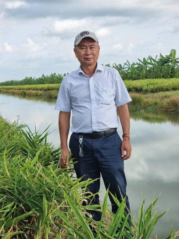 Anh Khánh đứng bên bờ kênh, sau lưng là ruộng và vườn chuối